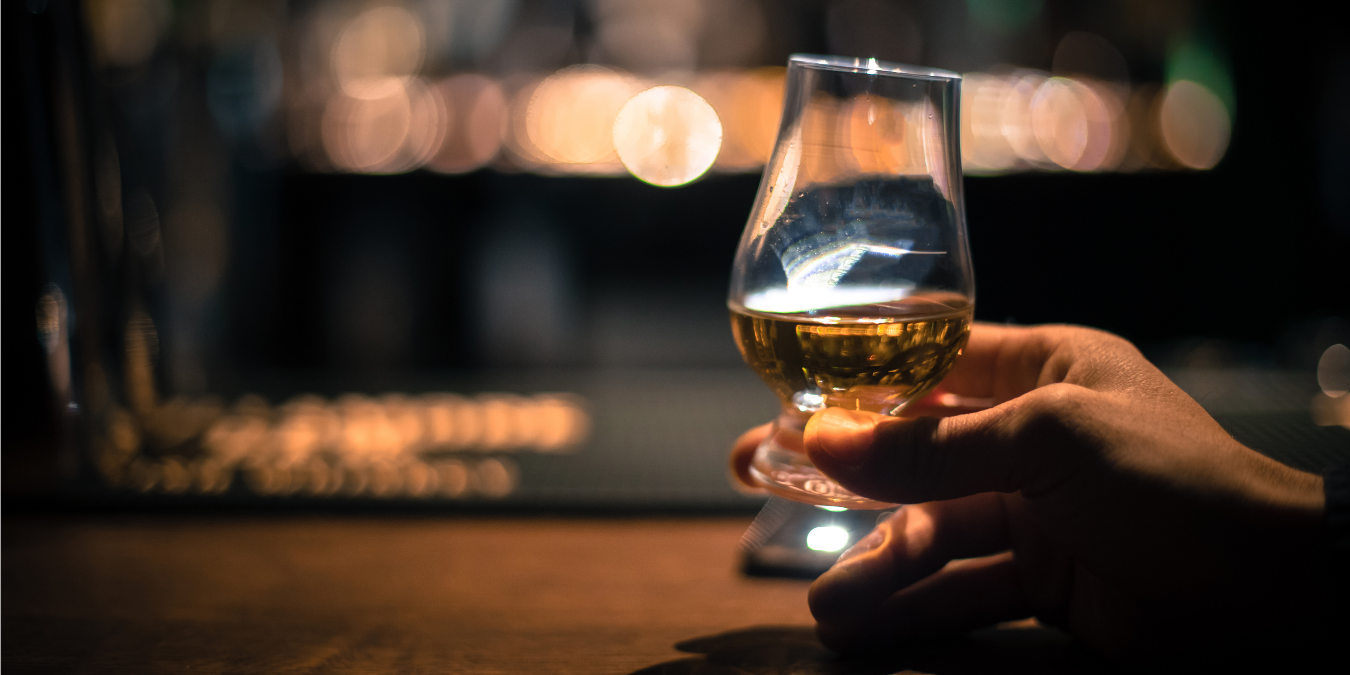 Hand holding a glass of whiskey with a blurred bar background