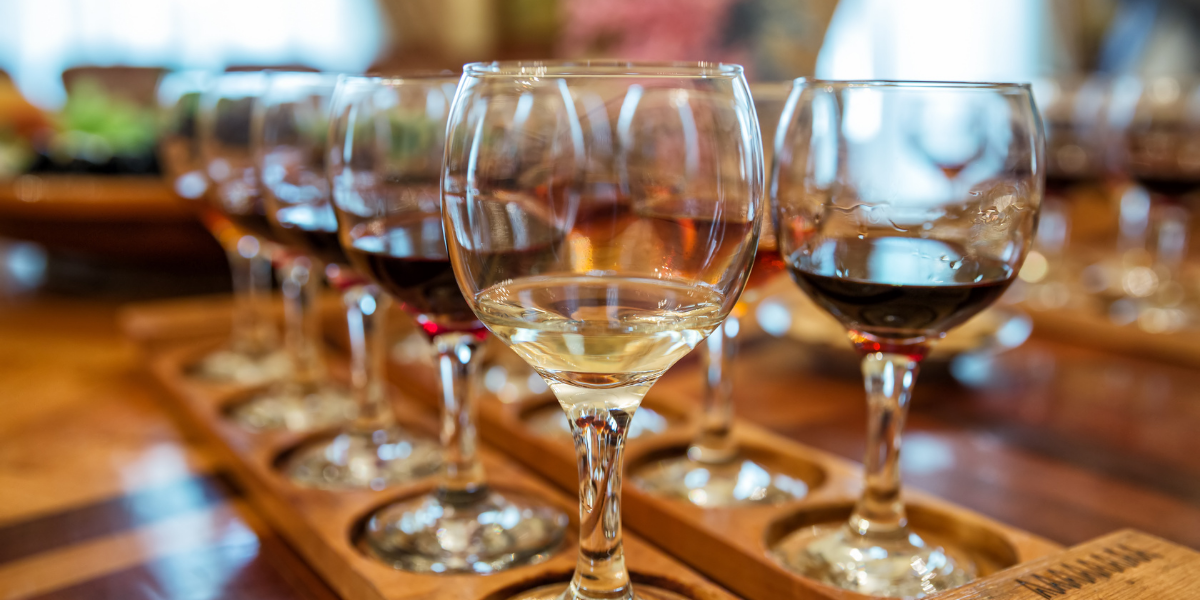 Row of wine glasses with different types of wine on a wooden tray.