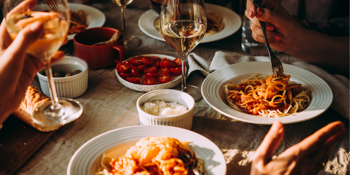 People enjoying a meal with pasta and wine at a table.