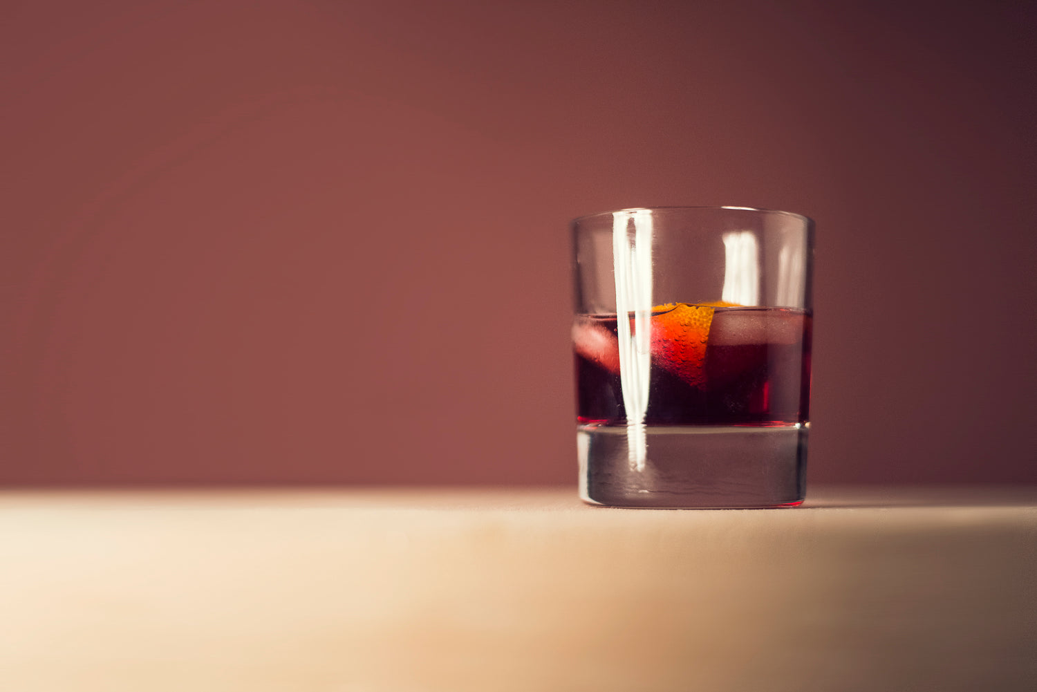 Classic Old Fashioned Cocktail with ice sitting on a counter with a deep red background